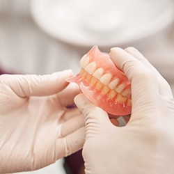 A close-up of gloved hands holding dentures