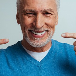 A senior patient pointing to his new and pretty dentures