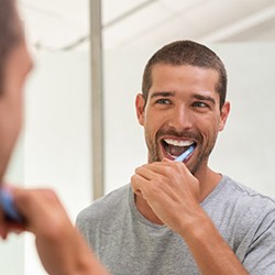 a man carefully brushing his teeth after gum disease treatment