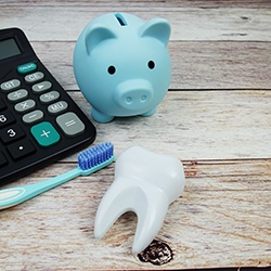 Calculator, toothbrush, model tooth, and piggy bank on wooden surface